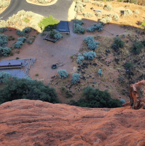 Aerial view of a desert landscape with rocky terrain, sparse vegetation, and a winding road in the background.